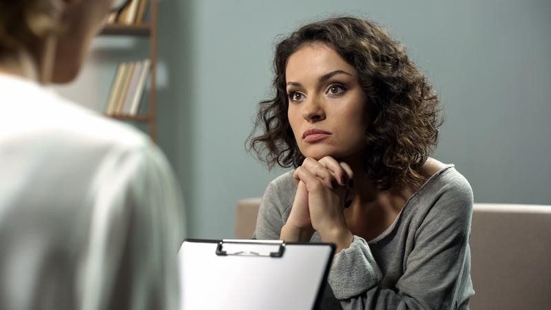 A woman is sitting on a couch talking to a doctor.